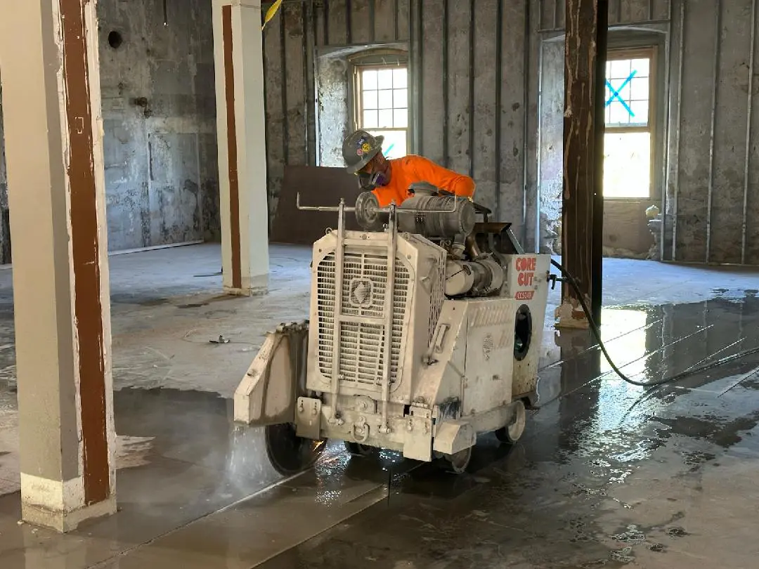 Worker operating concrete cutting machine indoors.