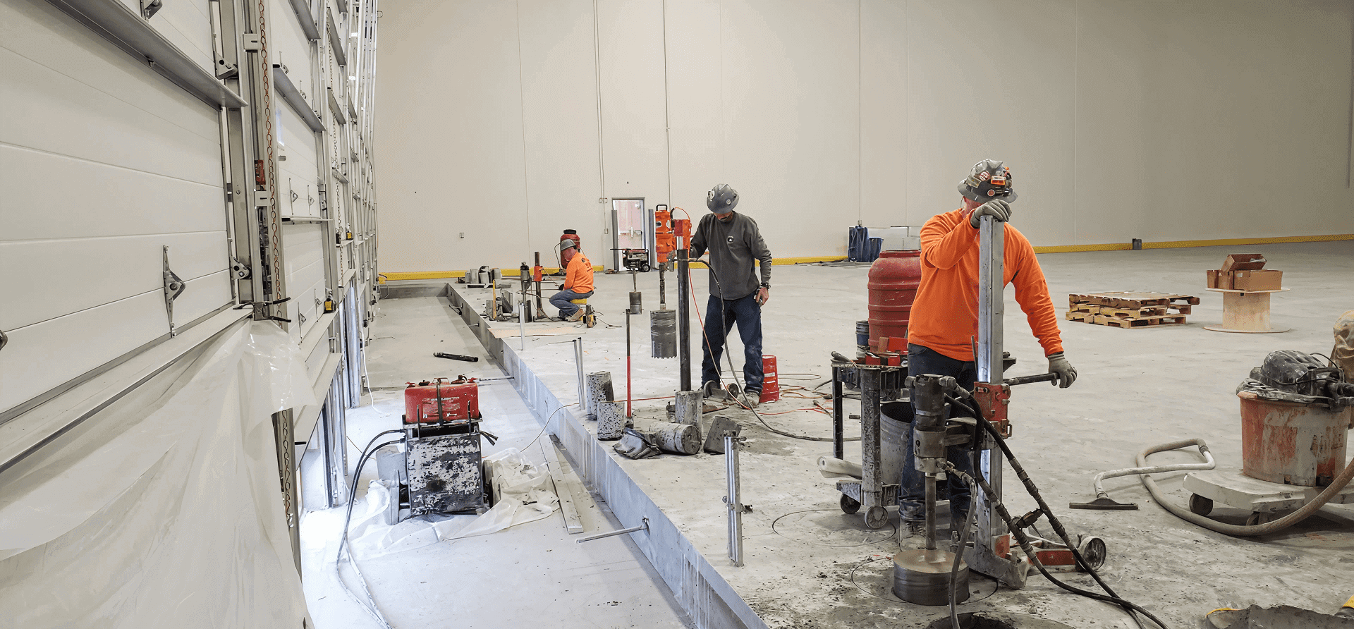 Construction workers drilling on indoor concrete floor.