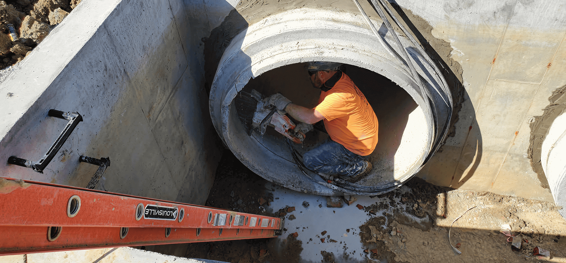 Worker cutting concrete pipe with saw.